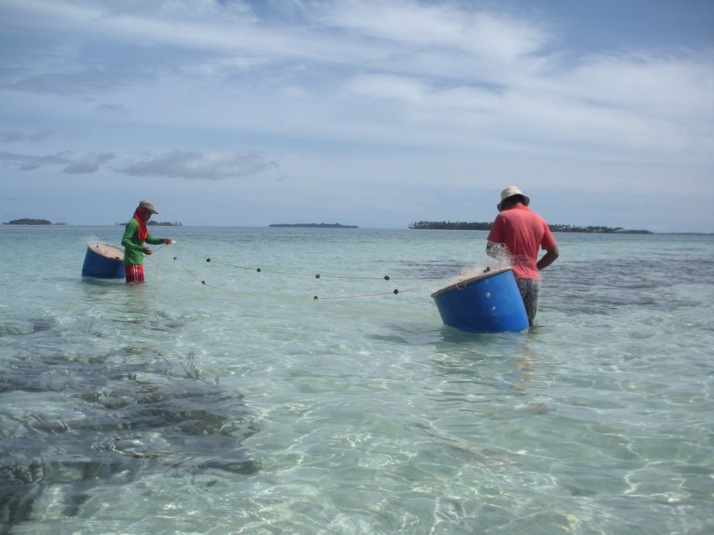 Two fishers deploy a net in shallow waters.